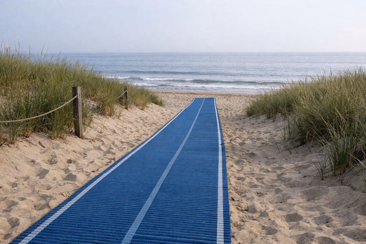 A blue roll-out beach access mat running from a dune path across the sand toward the ocean