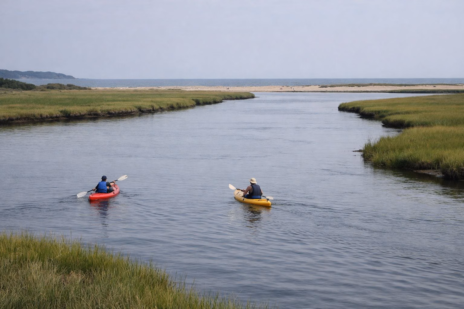 Two kayakers paddling a calm tidal river between salt marsh banks toward the sea