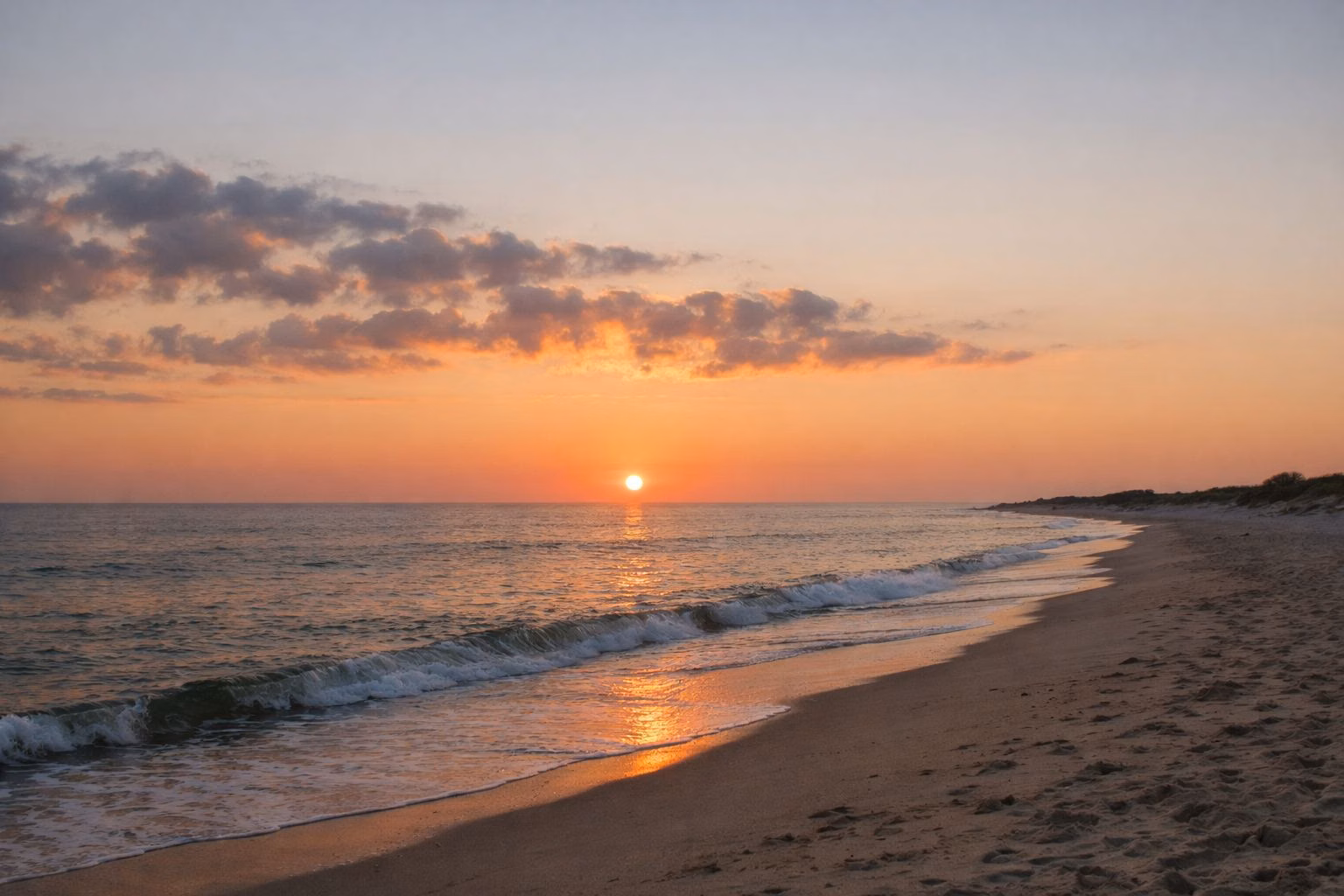 The sun rising over the ocean from an empty sandy beach, low clouds lit orange