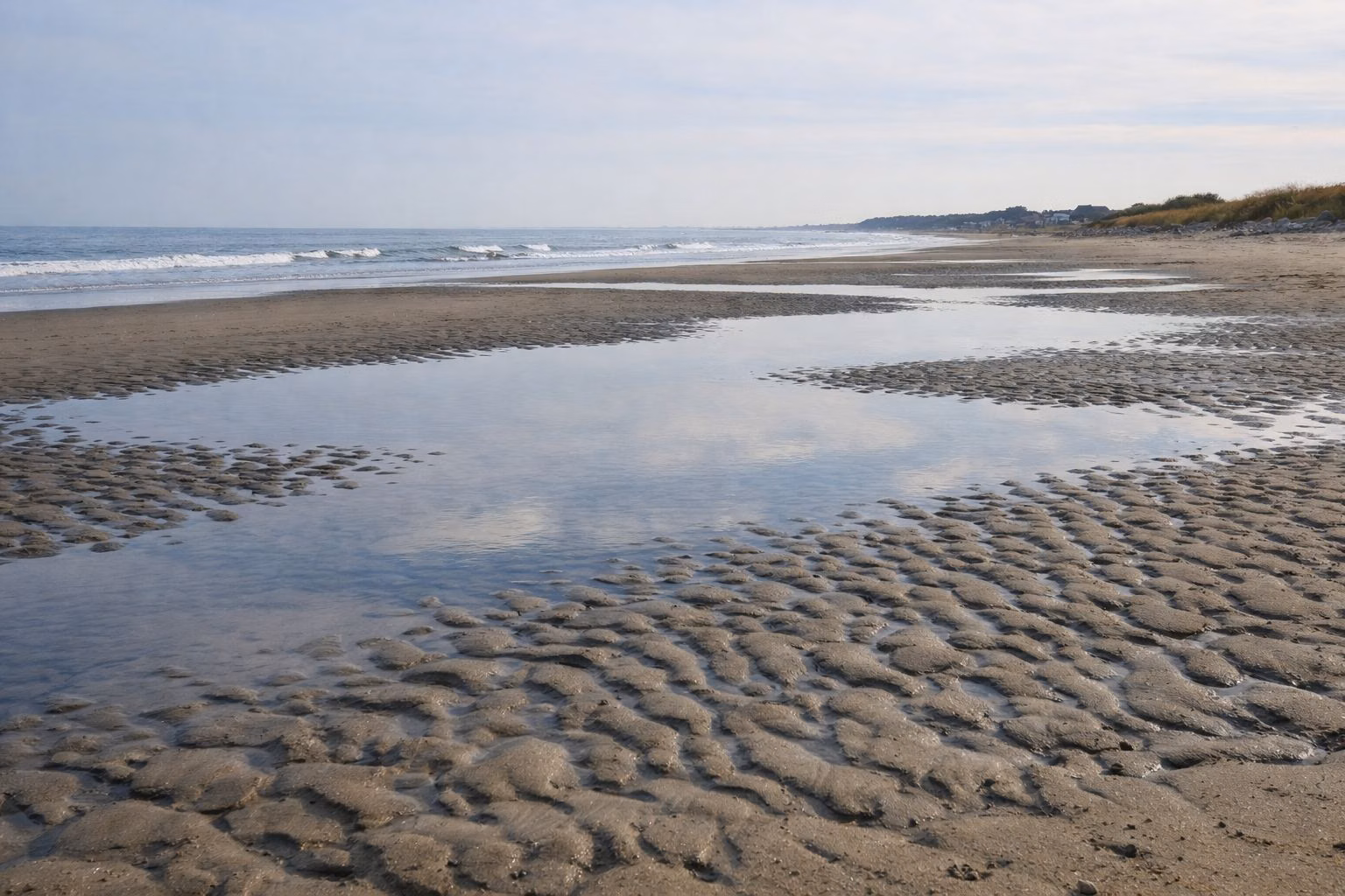 Rippled wet sand and a shallow tide pool reflecting the sky on an ocean beach at low tide